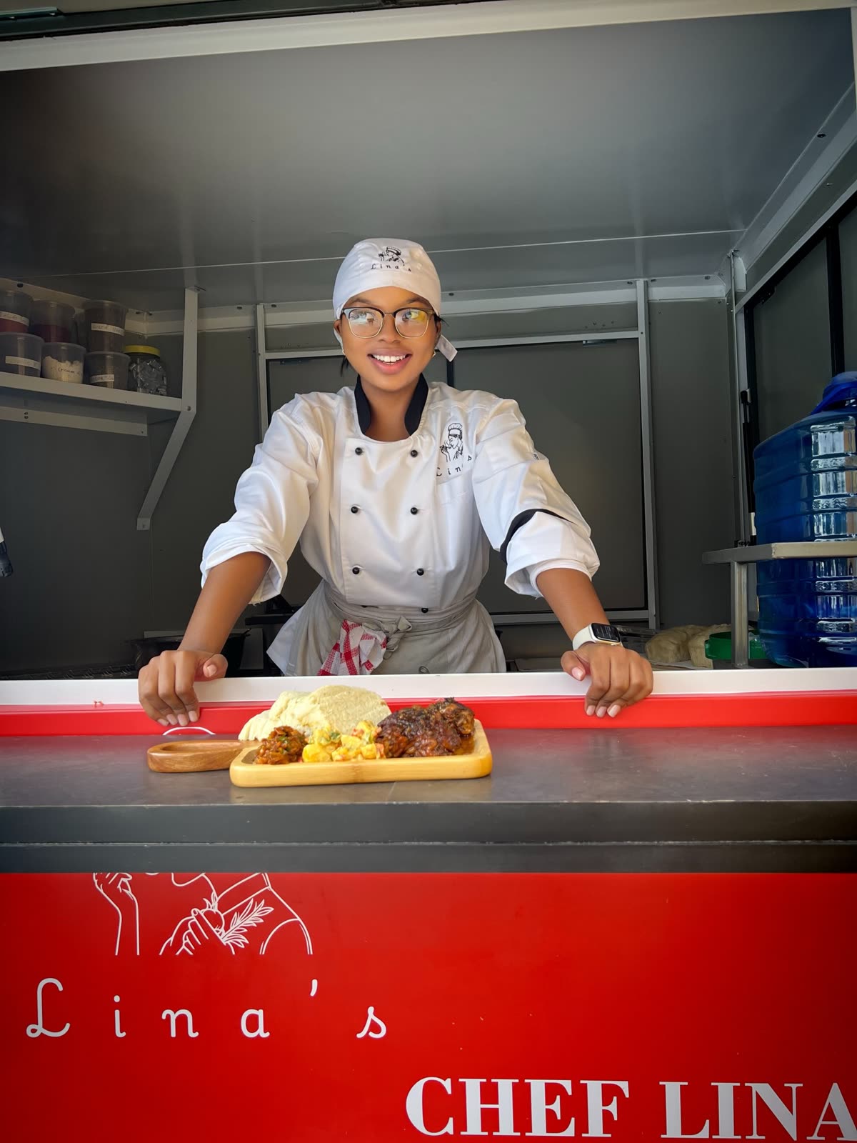 Chef Lina inside her mobile kitchen trailer, presenting a plated meal